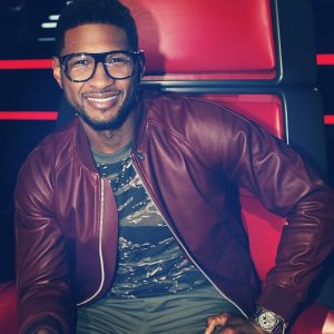 Usher wearing a pair of large, thick-frame glasses to support his last remaining contestant on NBC's The Voice. 